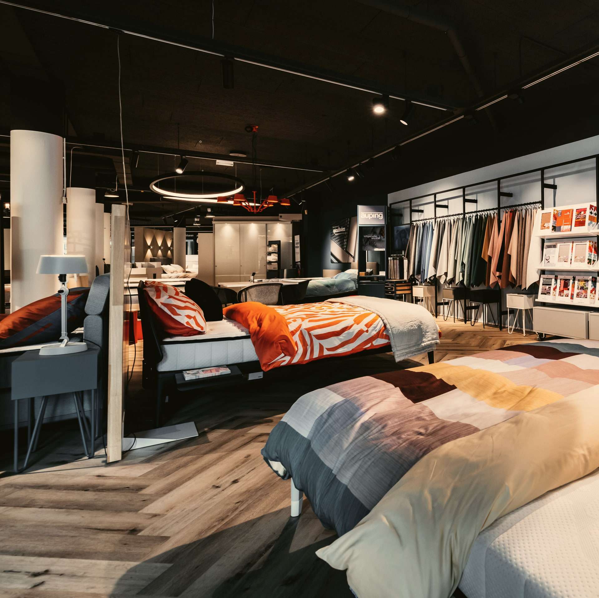 De slaapafdeling van Wielinga & Tabbers: opgemaakte bedden en boxsprings op een visgraatvloer, met een rek bedtextiel en lampen boven de bedden